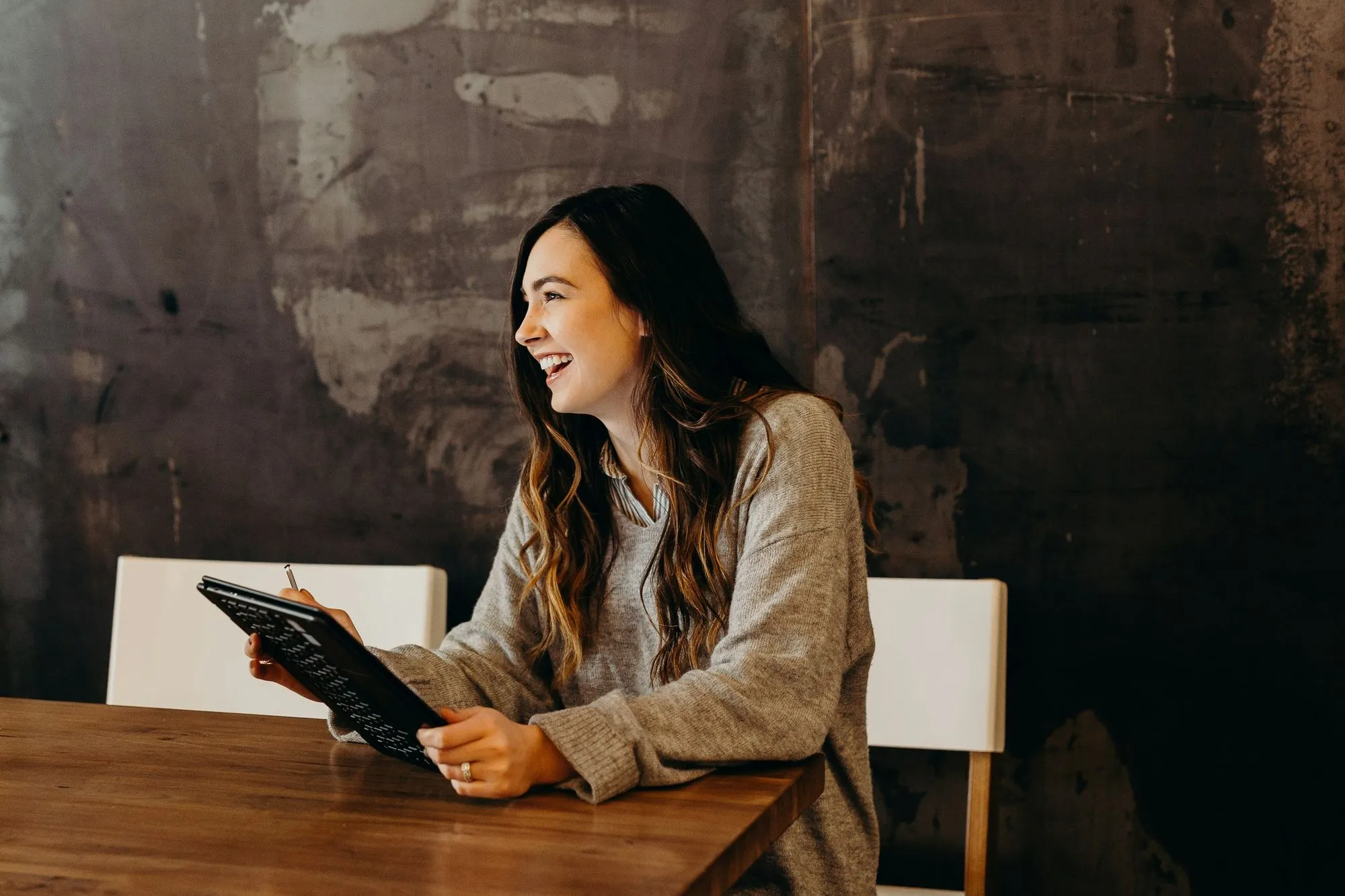 A woman sitting on a chair at a table holding a file and smiling.