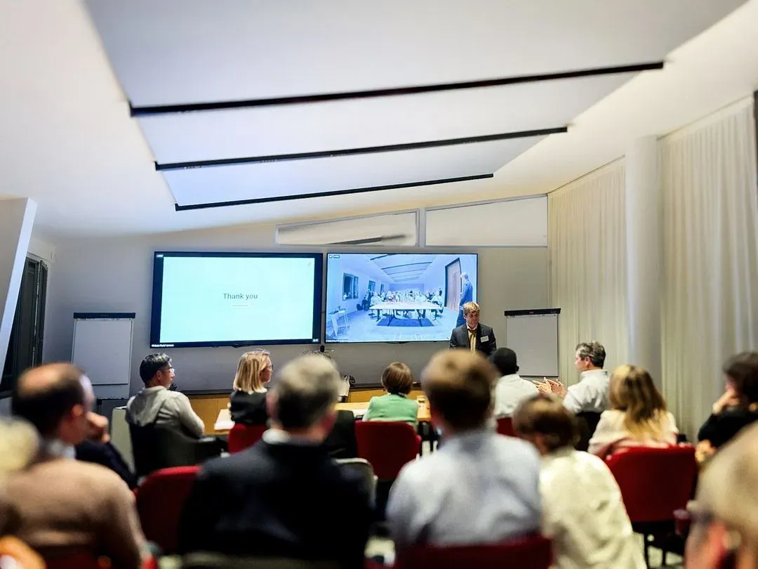 Public assis dans une salle de conférence regardant le pitch Alis Exchange projeté sur deux grands écrans lors de la HBS Alumni New Venture Competition à Paris