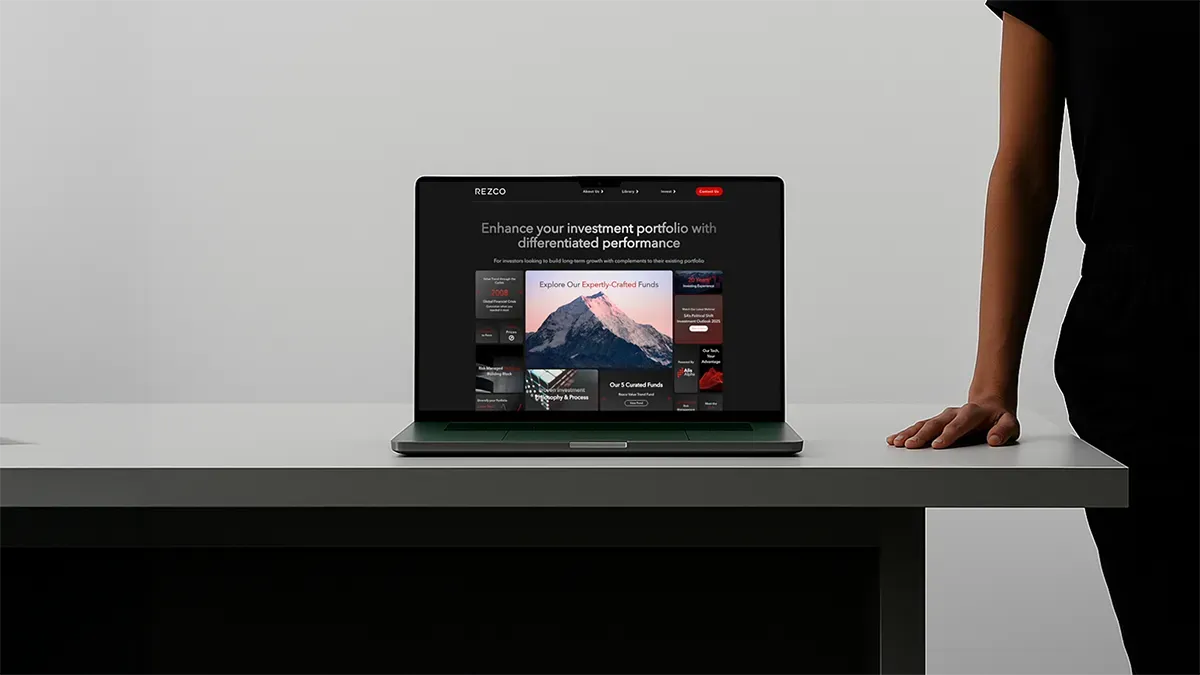 Laptop displaying an investment portfolio website on a white desk with a person standing beside it.