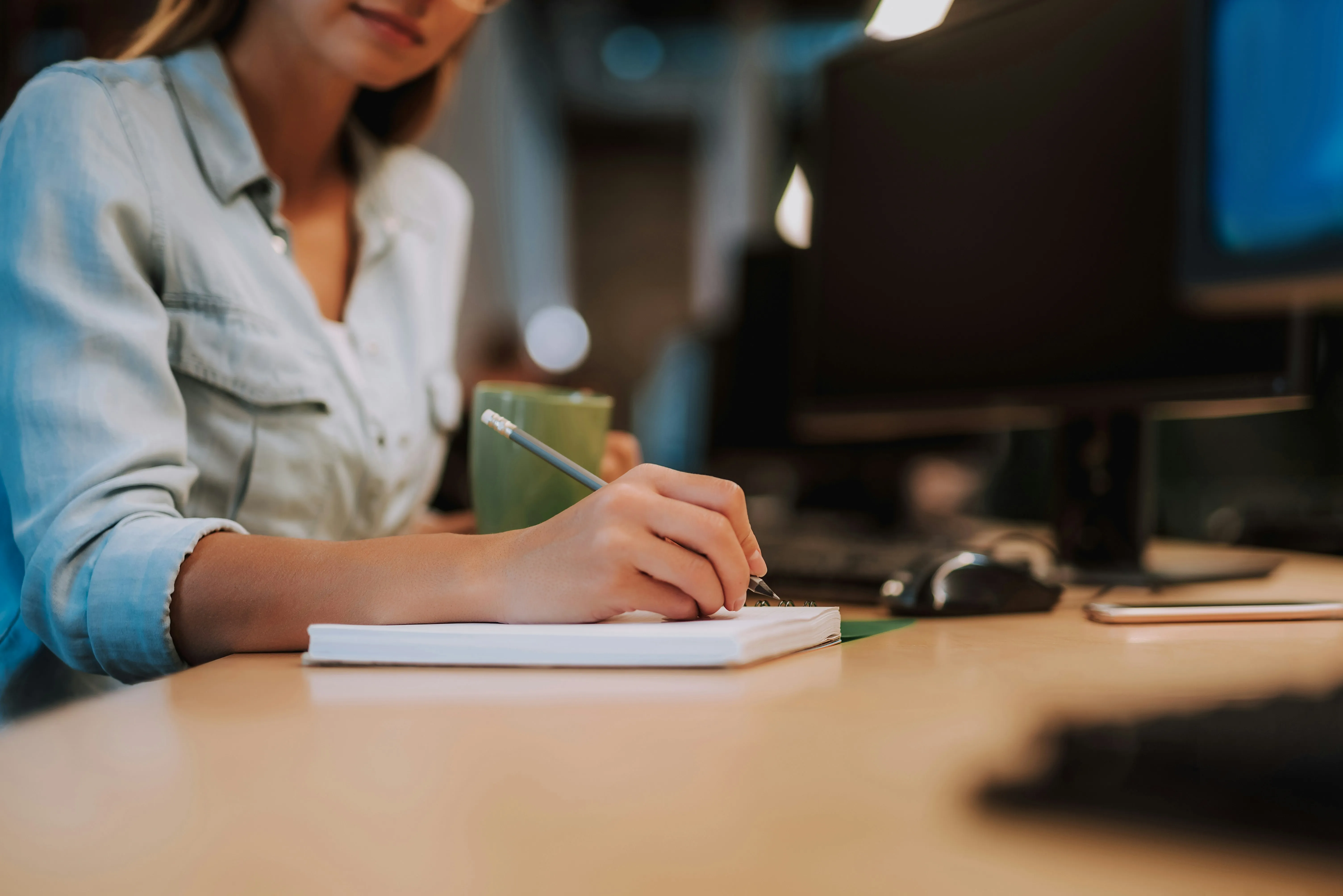 A woman writing notes on a piece of paper at her desk.