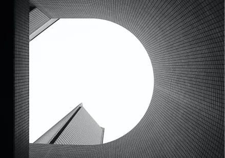 Black and white photo of the sky and a building taken from below through the opening of another building.