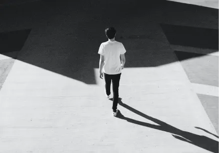 Overhead black and white photo of a person in a white t shirt walking across a cement pavement.